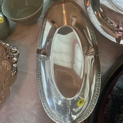 Sale Photo Thumbnail #99: Vintage silver-plated oval serving dish featuring an ornate leaf-and-bead border, shown alongside other silver tableware and ceramic bowls.