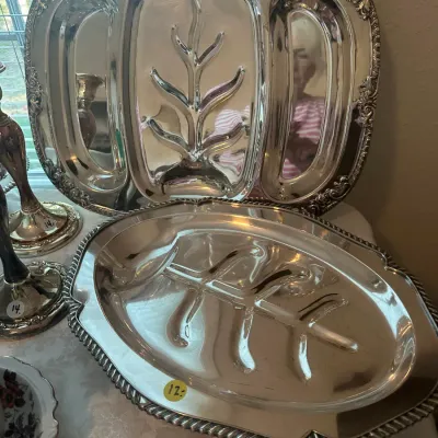 Sale Photo Thumbnail #98: Two vintage silver-plated meat platters, including a divided platter with an ornate scroll border and a classic tree-and-well platter with a gadroon edge.