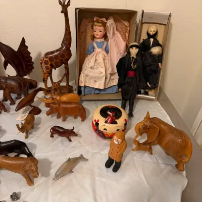 Sale Photo Thumbnail #76: Collection of vintage dolls, including a boxed mid-century doll in a blue dress, displayed alongside an assortment of hand-carved wooden animal figurines.
