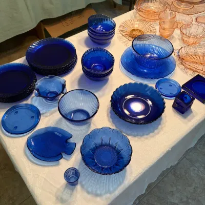 Sale Photo Thumbnail #57: Vintage cobalt blue glassware collection featuring plates, nested bowls, and a fish-shaped dish, displayed alongside pink depression glass pieces.