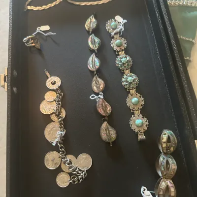 Sale Photo Thumbnail #119: Collection of vintage silver-tone jewelry displayed in a black case, featuring an abalone shell leaf bracelet, a coin charm bracelet, and a turquoise-colored filigree link bracelet.