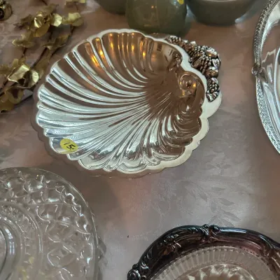 Sale Photo Thumbnail #101: Vintage silver-plated shell-shaped serving dish featuring a decorative grape cluster handle, displayed alongside other glassware and ceramics.