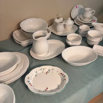 Sale Photo Thumbnail #60: Assorted white ceramic tableware and serving pieces with embossed details, including pitchers, bowls, plates, and a single holiday plate with a holly and berry motif.