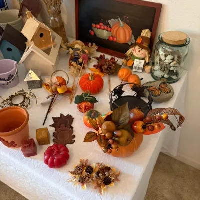 Sale Photo Thumbnail #90: Collection of autumn and Thanksgiving-themed home decor, featuring faux pumpkins, a scarecrow doll, small wooden birdhouses, a framed pumpkin painting, and various seasonal accents.