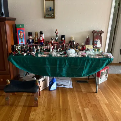 Sale Photo Thumbnail #19: Collection of vintage Christmas decorations, including various wooden nutcrackers, figurines, and holiday ornaments displayed on a table, with a small camel saddle stool in the foreground.