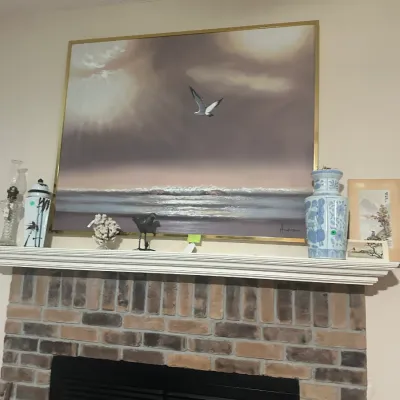 Sale Photo Thumbnail #103: Large framed coastal painting depicting a seagull flying over waves, signed 'Andrew', displayed on a mantel alongside blue and white ceramic vases, a glass oil lamp, and other decorative accents.