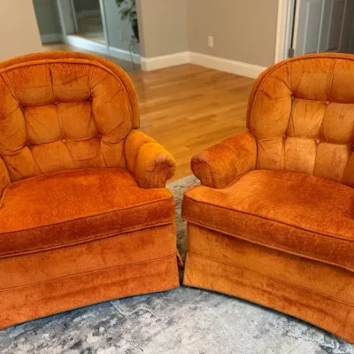 Pair of vintage tufted orange velvet armchairs featuring a tailored skirt and button detailing.