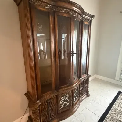 Large, ornate wooden china cabinet featuring glass upper doors and intricately carved lower panels.