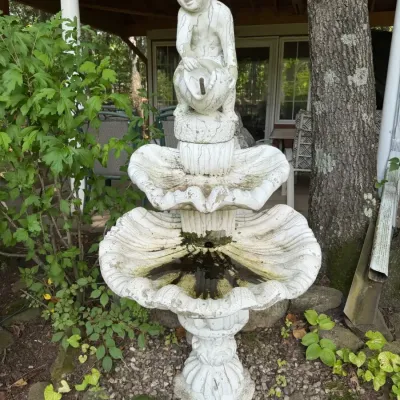 Vintage cast stone tiered garden fountain features a cherub pouring water from a jug
