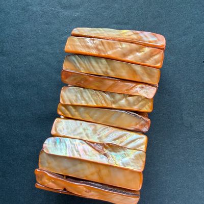 wide stretch cuff bracelet featuring glossy, rectangular shell panels in vibrant orange and amber tones with a natural iridescent sheen