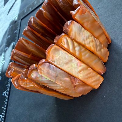 wide stretch cuff bracelet featuring glossy, rectangular shell panels in vibrant orange and amber tones with a natural iridescent sheen