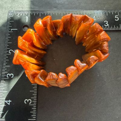 wide stretch cuff bracelet featuring glossy, rectangular shell panels in vibrant orange and amber tones with a natural iridescent sheen