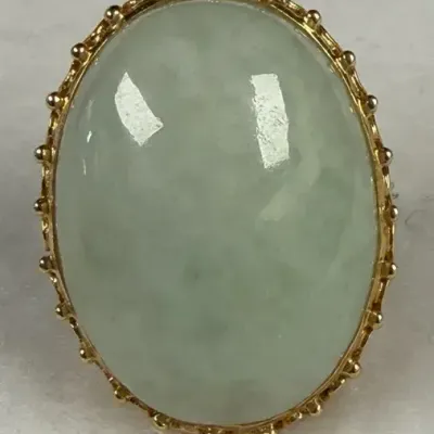 Oval cabochon jade ring set in a 14k yellow gold frame with a decorative prong or beaded edge border