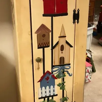 Tall Yellow Cabinet With Birdhouses Painted On It (61.5” H X 17.5” W X 12” D)