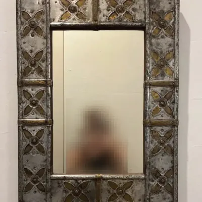 Vintage metal-clad wall mirror featuring a decorative frame with embossed floral or quatrefoil-like 