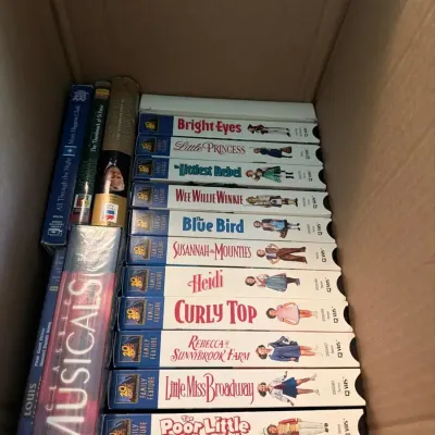 Assorted vintage media collection featuring VHS tapes of classic films and musicals along with a sel
