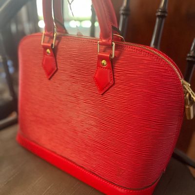 Louis Vuitton Alma handbag in red Epi leather, featuring gold-tone hardware and dual rolled top handles.