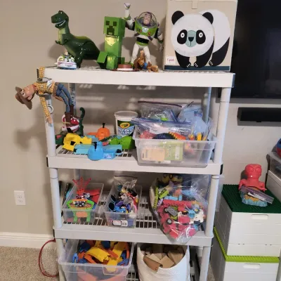 Four-tier white plastic shelving unit filled with children's toys, including Toy Story action figures, building blocks, and storage...
