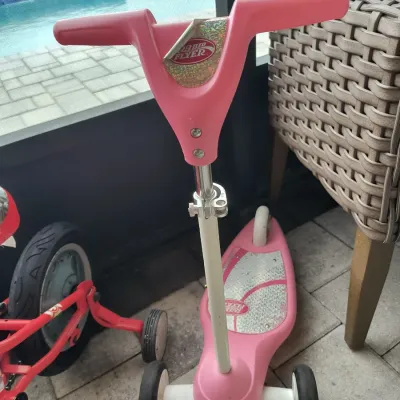 Radio Flyer pink three-wheel kick scooter with a glittery deck and adjustable handlebars, showing light wear from use.
