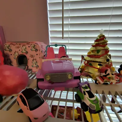 Assorted children's toys including a pink Barbie-style jeep, a small pink toy car, a Buzz Lightyear-themed vehicle, and a decorative...