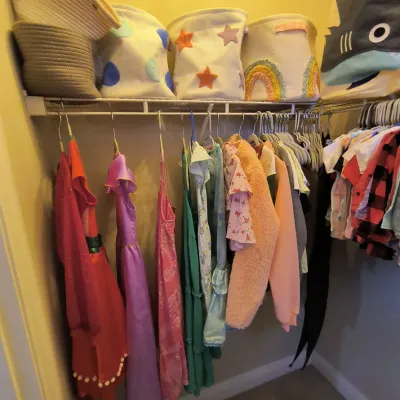 Assorted children's clothing, including dresses and jackets, hanging in a closet alongside decorative fabric storage bins.