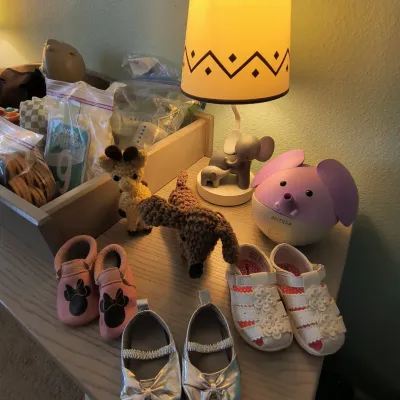 Assorted baby items including a dōTERRA elephant diffuser, an elephant table lamp, crocheted animal toys, and several pairs of infant shoes.