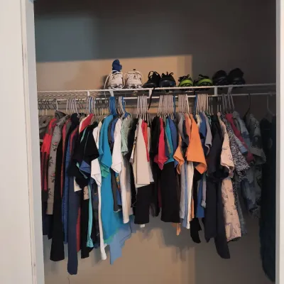 Assortment of children's clothing hanging on a wire closet rack, with several pairs of athletic shoes and cleats stored on the shelf...