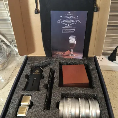 Daniau 12-piece cocktail smoker kit in its original packaging, including a torch, wood block, metal canisters, and instruction manual.