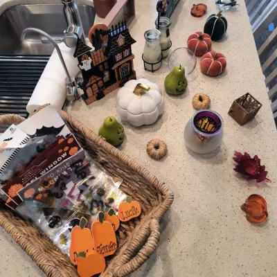 Assortment of autumn and Halloween decorations, including a woven basket filled with window clings, decorative pumpkins, a haunted house...