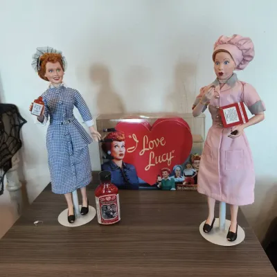 Two collectible "I Love Lucy" porcelain dolls on stands, featuring Lucy in her iconic Vitameatavegamin and chocolate factory...