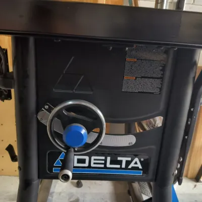 Delta table saw featuring a black metal frame, front-facing adjustment wheel with a blue center cap, and a clear bevel scale.