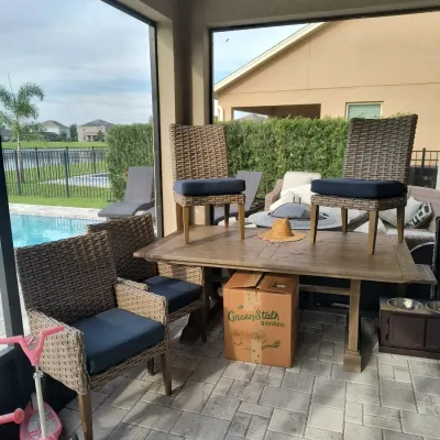 Outdoor dining set featuring a rectangular wooden table and four woven wicker chairs with navy blue cushions, shown on a screened-in patio.
