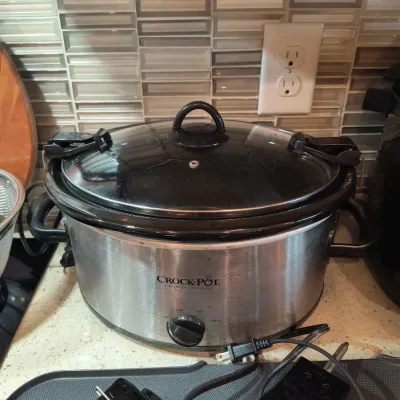 Crock-Pot stainless steel slow cooker with a locking glass lid, showing some light wear from use.