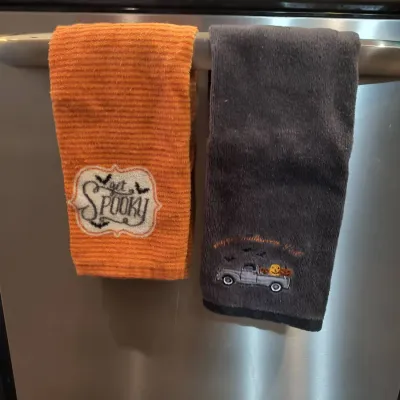 Pair of Halloween-themed kitchen hand towels, featuring an orange ribbed towel embroidered with "Get Spooky" and a dark gray...