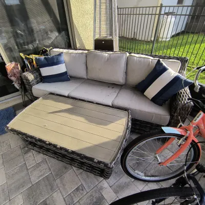 Outdoor wicker sofa with light gray cushions and blue-and-white striped accent pillows, paired with a matching wicker coffee table...