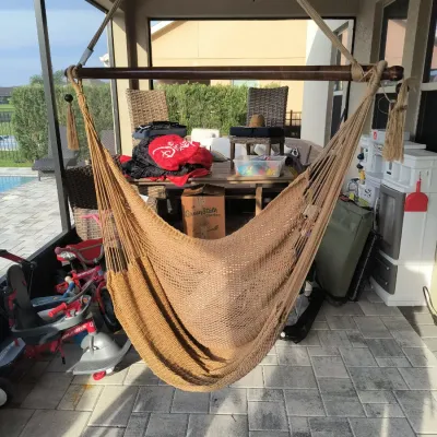 Woven rope hammock chair with a wooden spreader bar, suspended on a screened-in patio.