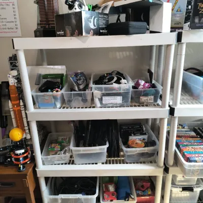 White plastic shelving unit holding various items, including electronics, cables, and model kits, organized in clear plastic bins.