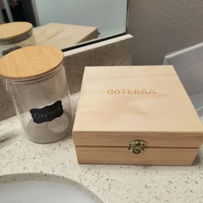 dōTERRA wooden essential oil storage box with a metal latch, shown next to a glass canister with a wooden lid labeled "Oxyboost".