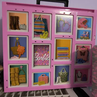 Vintage pink Barbie doll carrying case with molded plastic compartments displaying various outfits and accessories.
