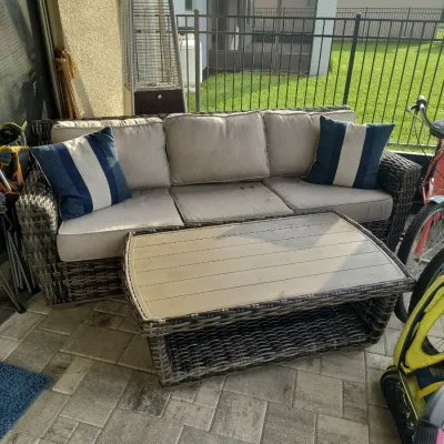 Outdoor wicker sofa and matching coffee table set, featuring beige cushions and two blue-and-white striped accent pillows.