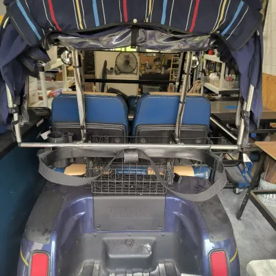 Rear view of a blue Yamaha golf cart featuring a striped canopy, rear basket, and blue and tan vinyl seats.