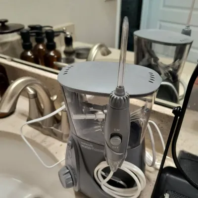 Waterpik countertop water flosser in gray and white, shown sitting on a bathroom vanity.