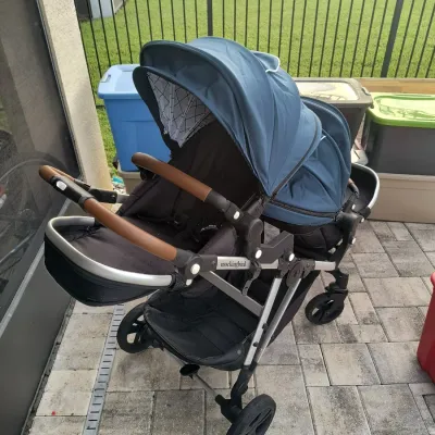 Mockingbird double stroller in blue and black with brown leatherette handles, showing light outdoor use.