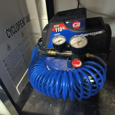 Campbell Hausfeld 110 PSI portable air compressor with dual pressure gauges and a coiled blue air hose.