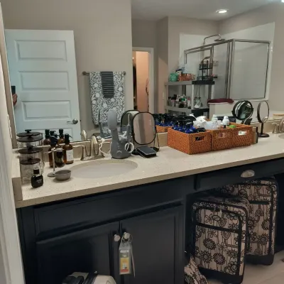 Bathroom vanity area featuring a dark-painted cabinet with a light-colored countertop, dual sinks, a large mirror, and various personal...
