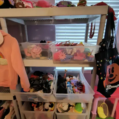 White plastic three-tier shelving unit filled with clear storage bins containing various children's toys, dolls, and accessories.