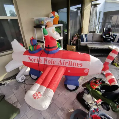 Large inflatable Christmas decoration featuring Santa Claus piloting a red and white "North Pole Airlines" airplane, shown...