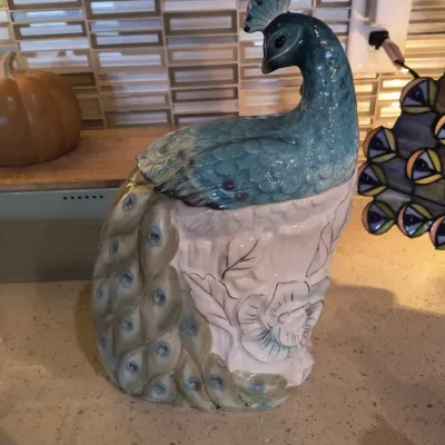 Vintage ceramic peacock cookie jar featuring a blue-glazed bird perched on a white floral base with a draped tail.
