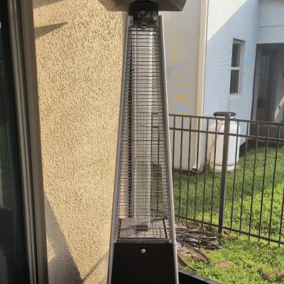 Pyramid-style outdoor patio heater with a stainless steel frame and protective safety grill, showing some light outdoor wear.