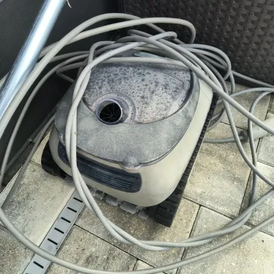Robotic pool cleaner with power cord, showing signs of outdoor use and weathering.